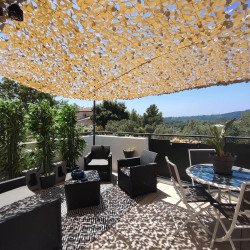 Filet de camouflage beige ombrageant une terrasse avec vue sur les collines