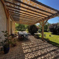 Ombre filtrée par un filet de camouflage beige sous une pergola en bois