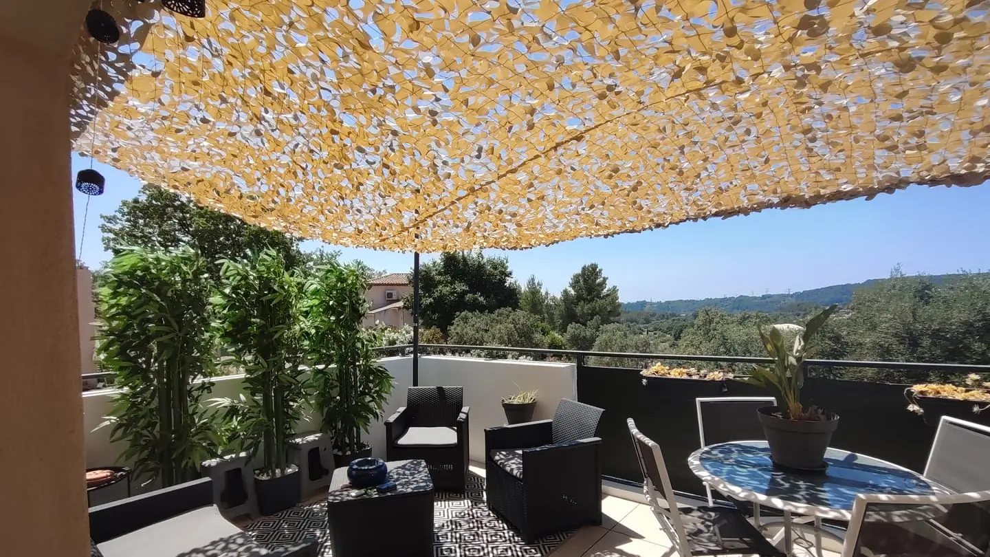 Filet de camouflage beige ombrageant une terrasse avec vue sur les collines