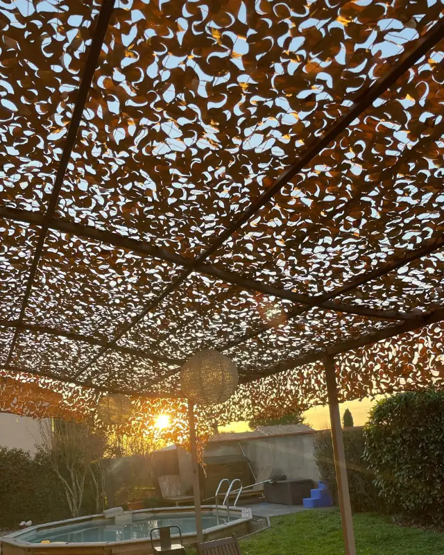 Soleil couchant filtré par un filet de camouflage tendu sur une pergola