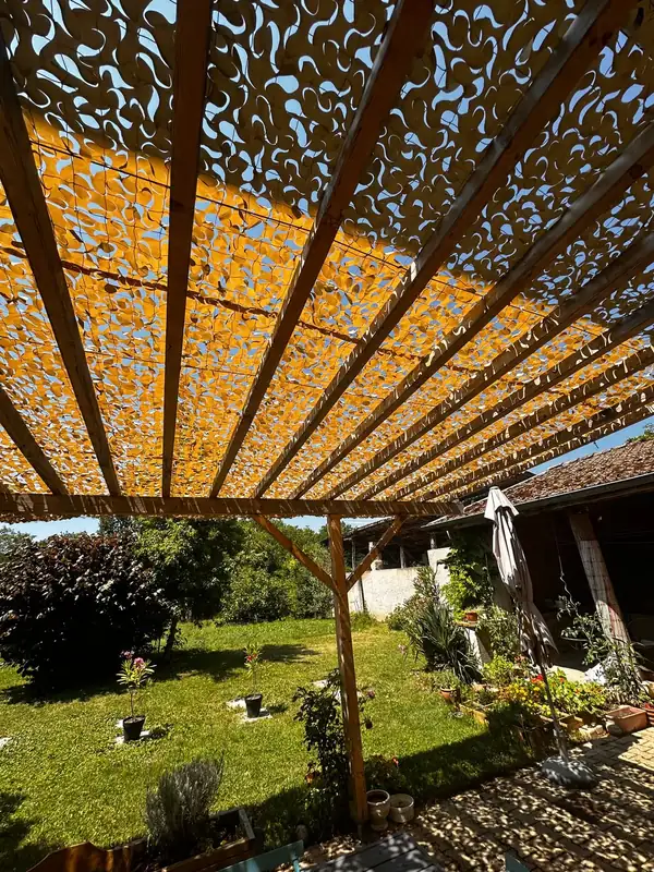 Lumière filtrée par un filet beige sur une pergola en bois
