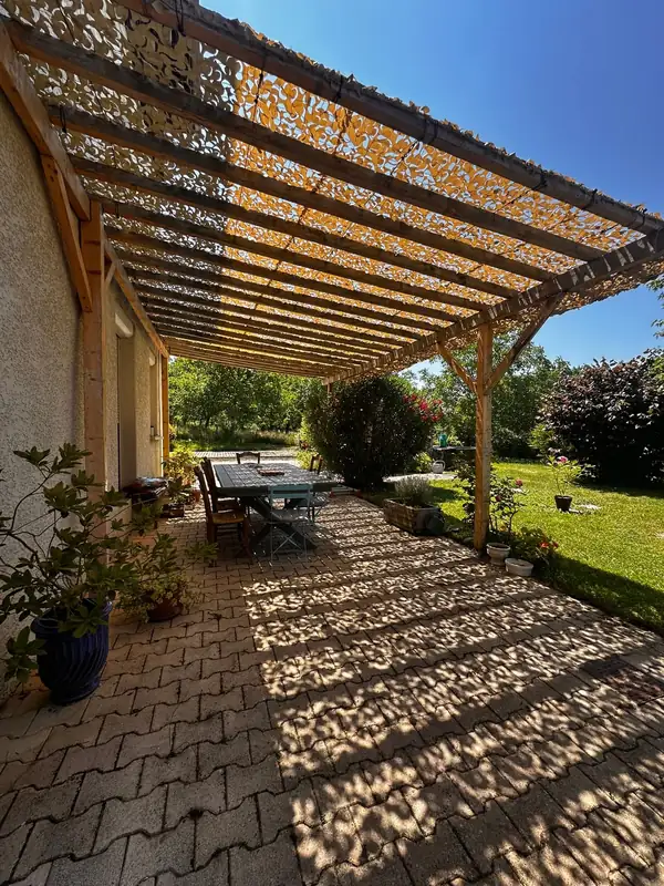Ombre filtrée par un filet beige sous une pergola en bois